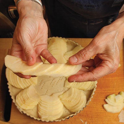 She then takes six or seven slices from the remaining apple and spreads them out lengthwise to form a narrow row of overlapping slices, which she arranges in an arc in the tart shell