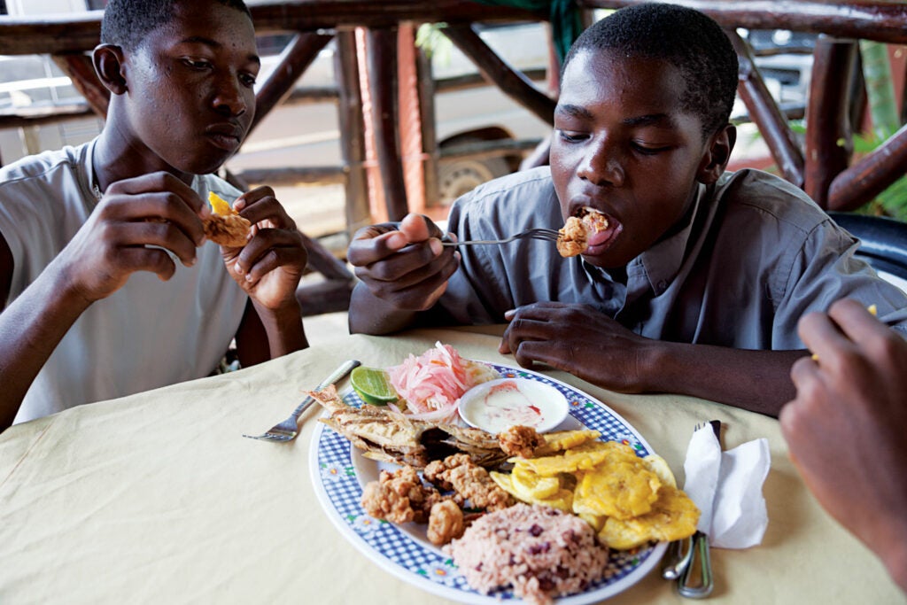 Boys enjoy a lunch of fried conch, kingfish, plantains, and rice and beans with coconut milk at Restaurante Corozal, in Corozal, Honduras
