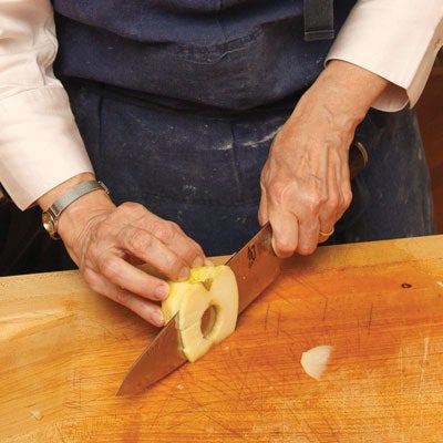 She trims the bud and stem ends, then stands the apple half on end to cut a thin layer from the cored side so that the slices fully separate but remain stacked together