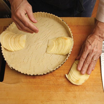 She returns the half to its flat side on the cutting board and covers it with her hand, pressing down until the mass of apple flattens into a neat row of overlapping slices