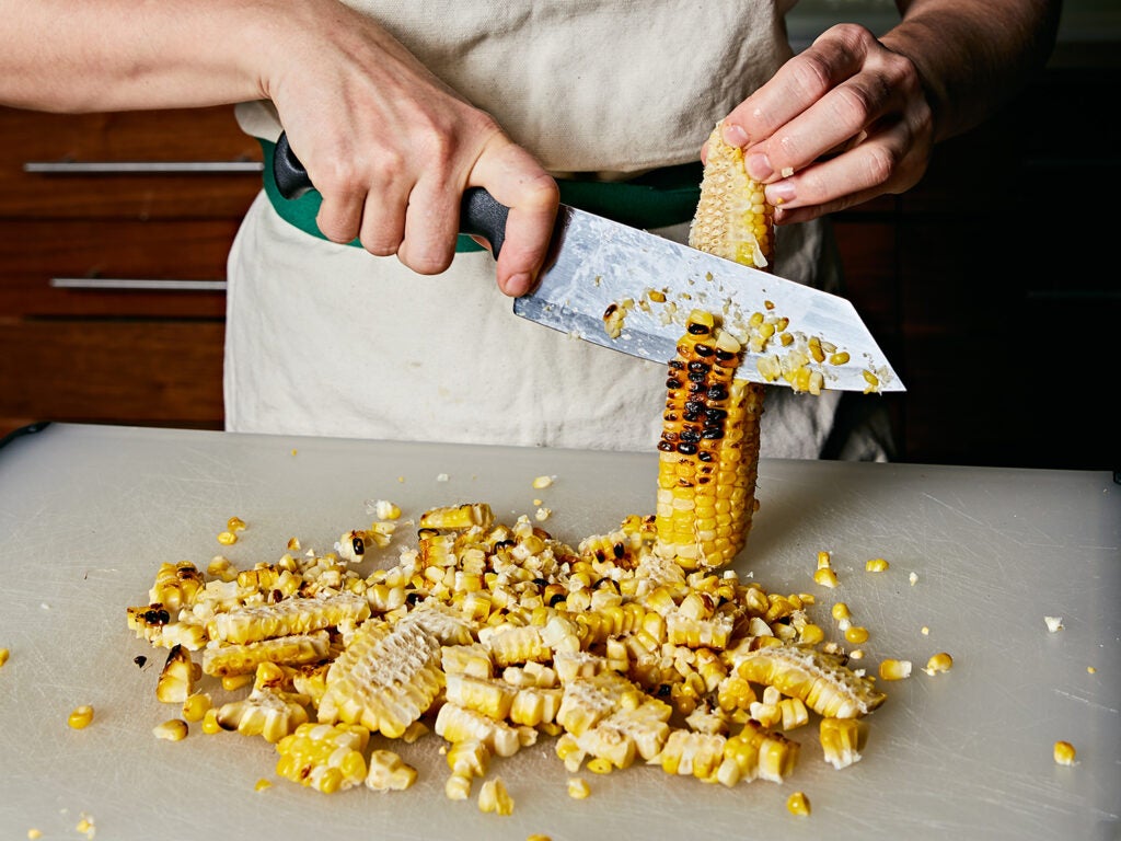 Cutting grilled corn kernels off the cob.