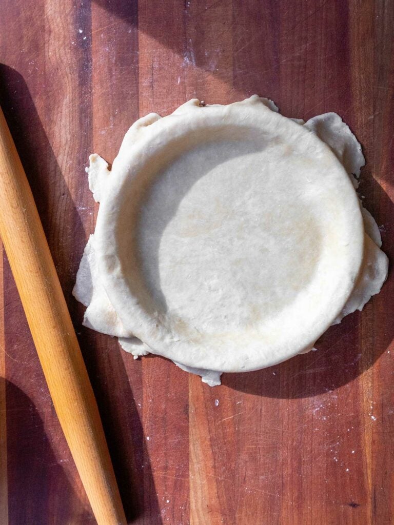 Pie crust in pie plate with rolling pin on countertop.