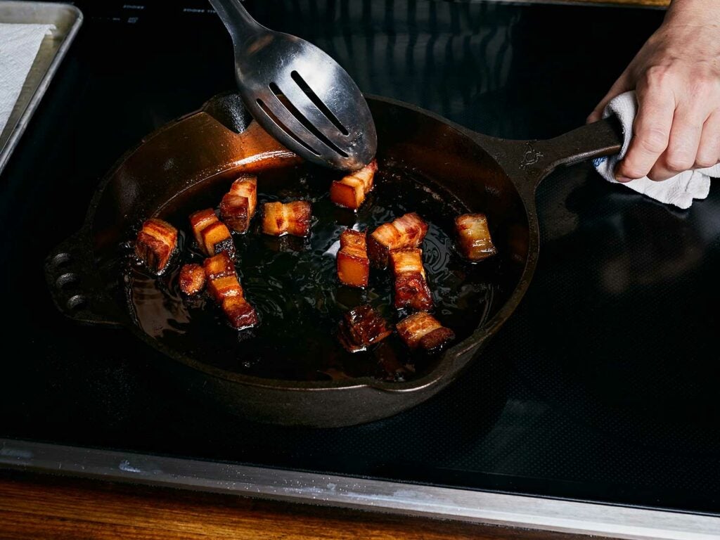 Cooking slab bacon in a hot cast-iron skillet with duck fat or butter until crisp.