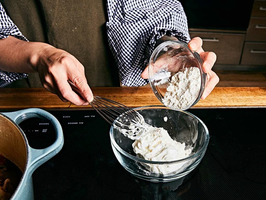 Whisking flour into sour cream to create a roux for the gravy.