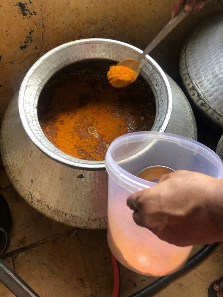 Maharaj adds red chili powder to the cauldron.