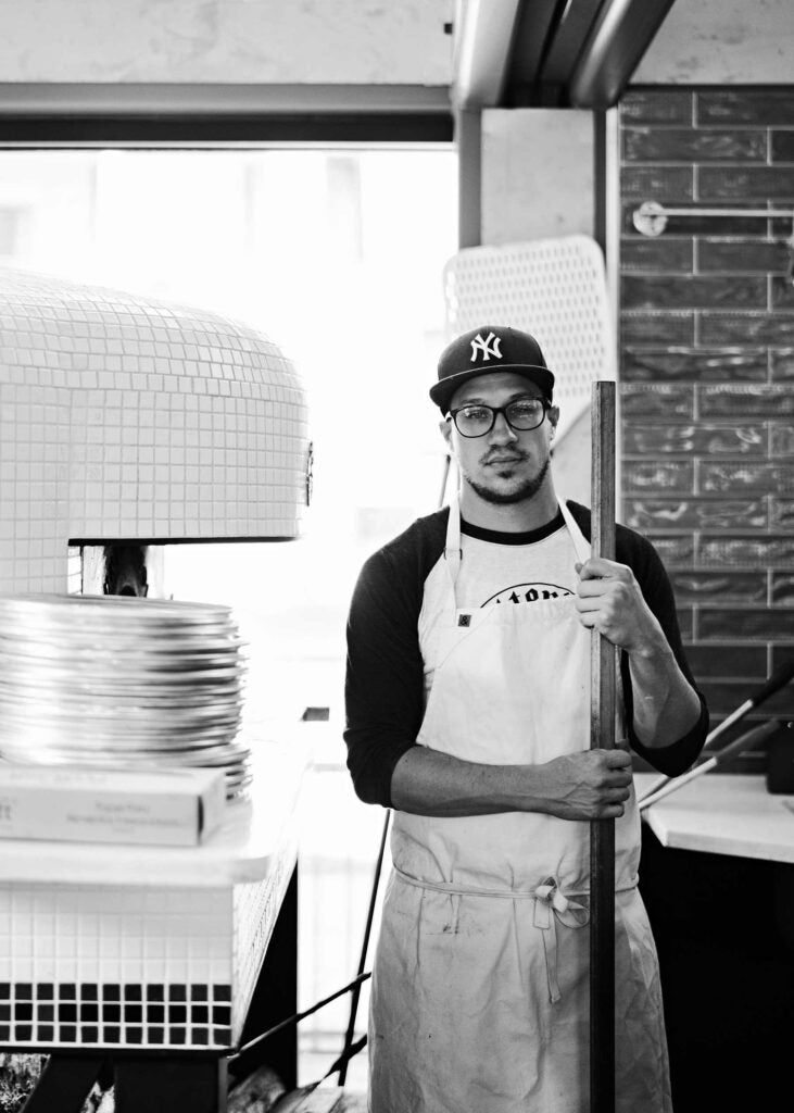 Chef Kyle Jacovino standing beside a pizza oven